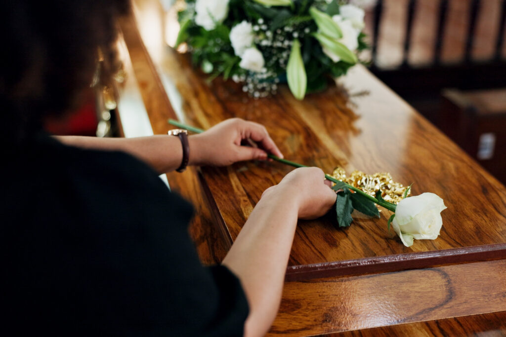 Hands, woman and rose at funeral for farewell, mourning death and goodbye at burial ceremony. Sad, female person and rip with flowers for casket respect, memorial service and emotional for loss.