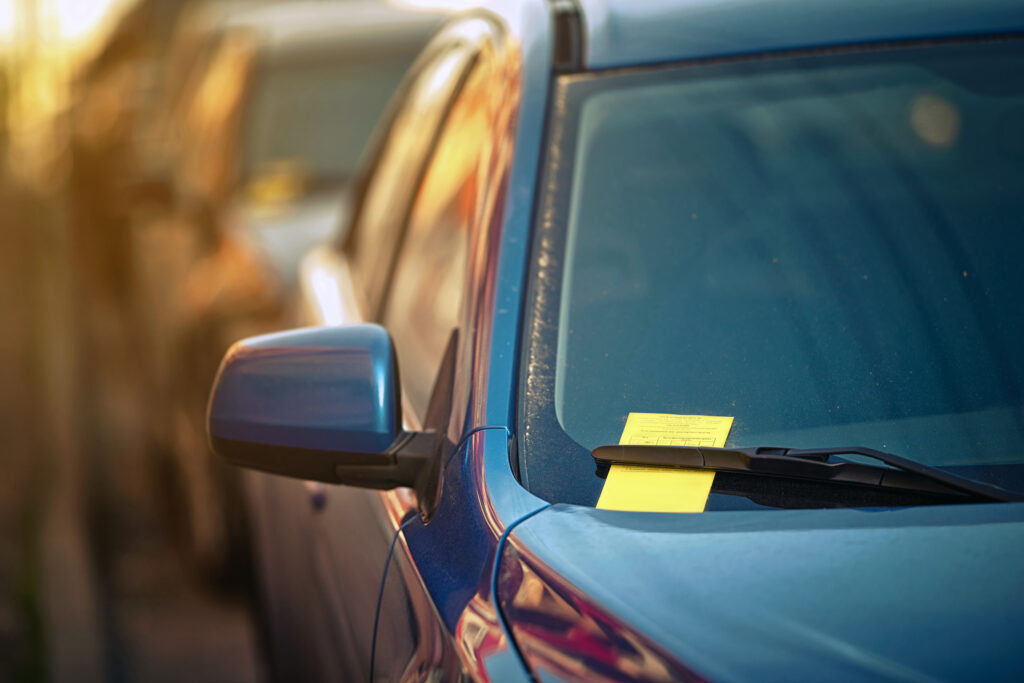 Yellow parking ticket over car windscreen wiper. Payment notice for parking penalty secured under car's windshield wiper. Parking charge notice