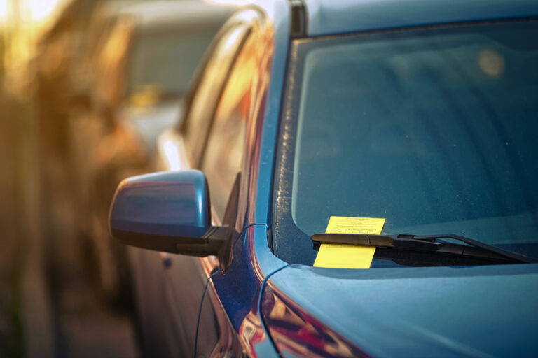 Yellow parking ticket over car windscreen wiper. Payment notice for parking penalty secured under car's windshield wiper. Parking charge notice