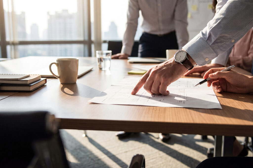 Close-up photograph of business professionals collaborating, with one person pointing at a document during a meeting.