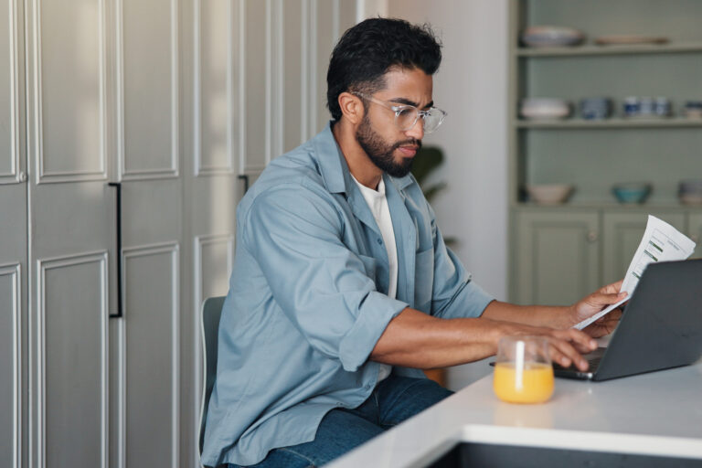 Home, paperwork and man with laptop, typing and writer with royalty statement, filing or calculation. Creative, author and person with document for self employment tax, online and financial analysis.